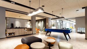 Un espace intérieur moderne comprenant une table de baby-foot, des coins salon et un comptoir d’accueil.