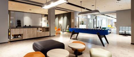 A modern indoor space with a foosball table, seating areas, and a reception desk.