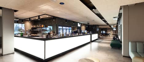 A modern bar area with a long counter, seating, and a projection screen.