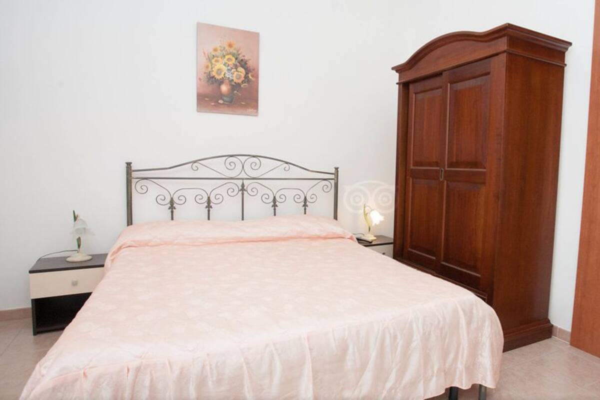 A bedroom with a bed, a nightstand, a wooden wardrobe, and two wall-mounted paintings.