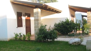 A two-story house with a stone facade, a wooden door, and a small garden with various plants. - Residence Gli Ulivi (Leverano)