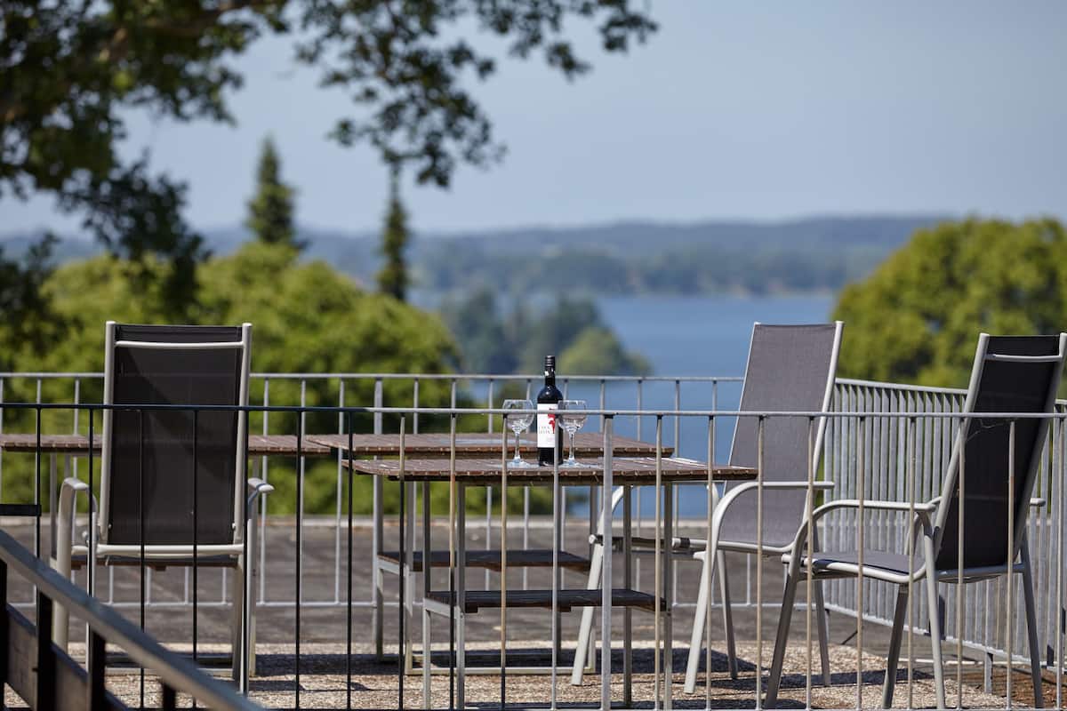 An outdoor seating area with metal chairs and tables, overlooking a body of water and greenery.