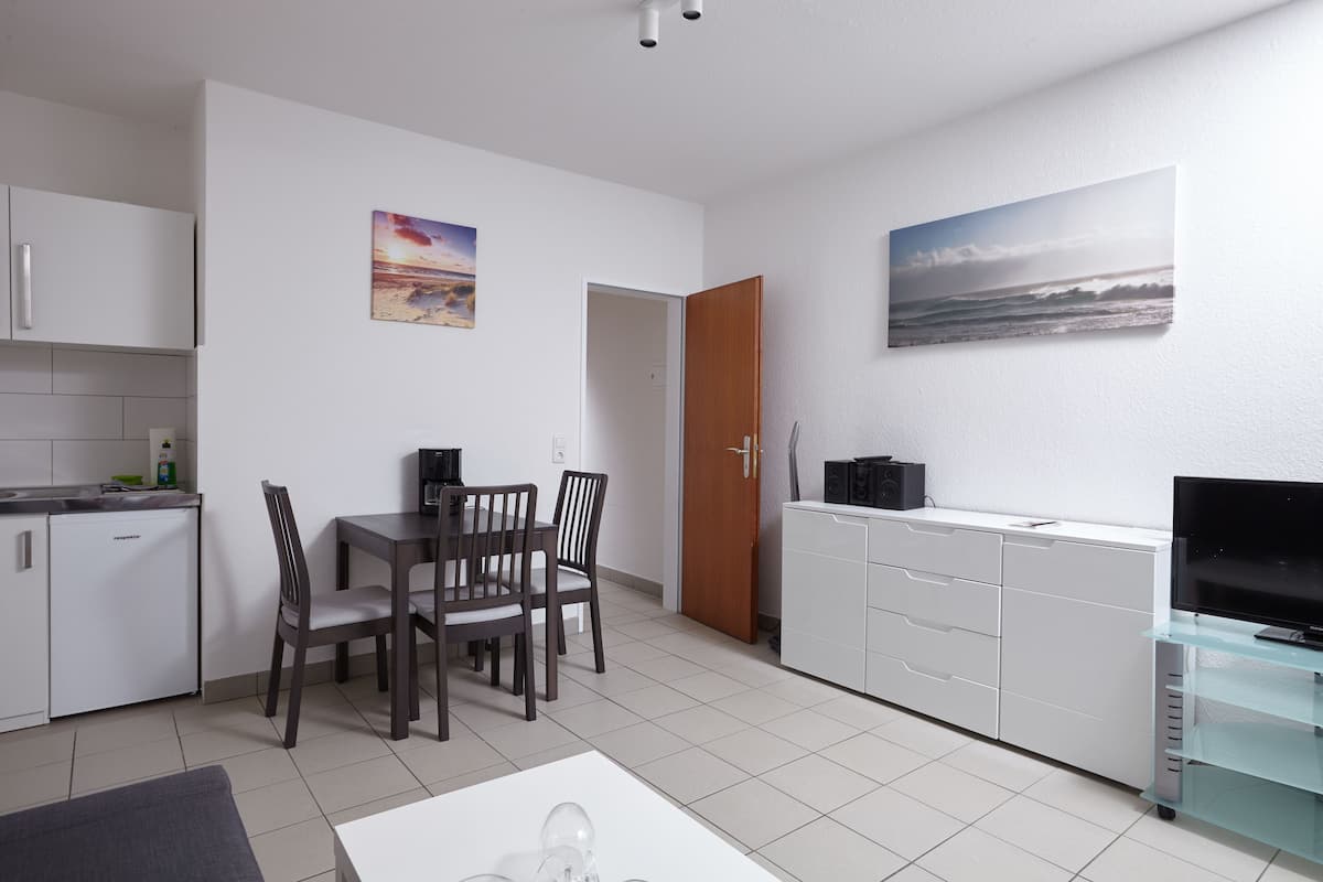 A modern kitchen with white cabinets, a dining area with a table and chairs, and a TV on a glass stand.