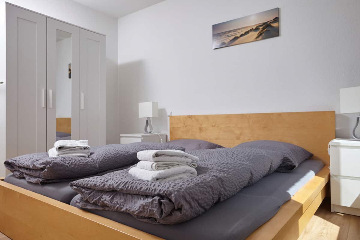A neatly made bed with a wooden headboard, a bedside table with a lamp, and a wardrobe with sliding doors.