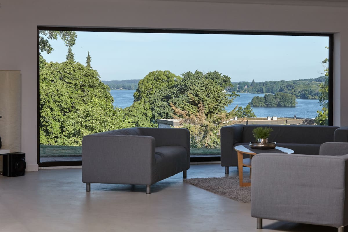 A modern living room with a large window offering a scenic view of a lake and forest.