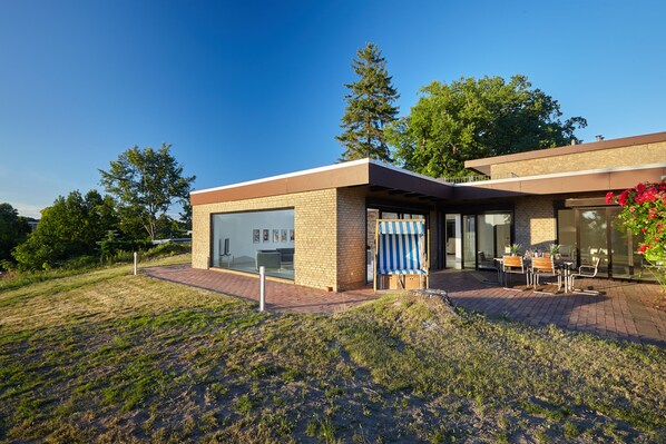 A modern house with a large garage, a covered patio with outdoor furniture, and a brick pathway leading to the entrance.
