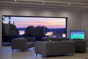 A modern living room with a large window offering a scenic view of trees and a body of water. There are two sofas and a flat-screen TV.