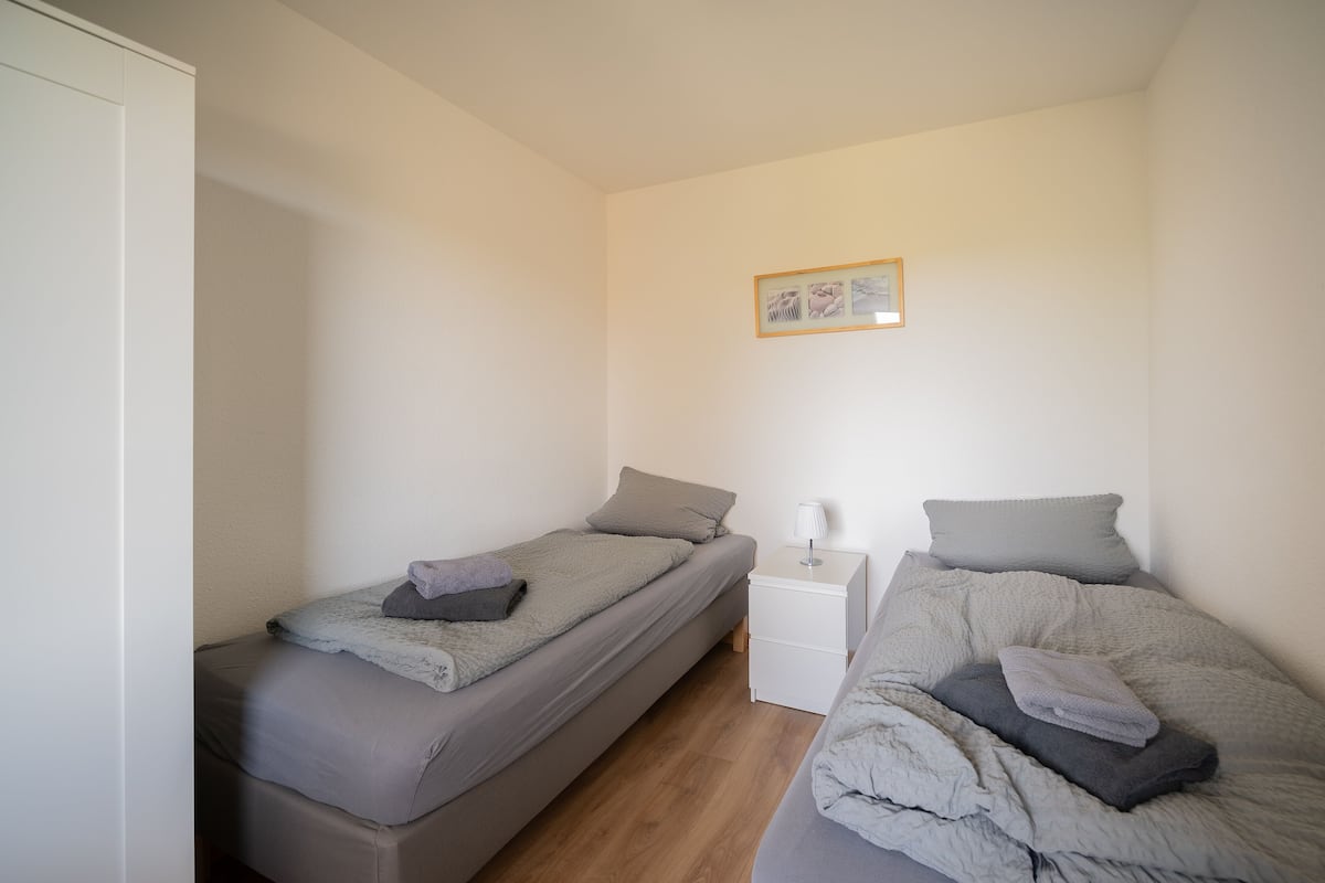 A small, clean room with two single beds, a nightstand with a lamp, and a framed picture on the wall.