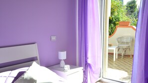 A bedroom with a bed, a nightstand, a lamp, and a view of an outdoor patio. - Bellatrix (Portici)