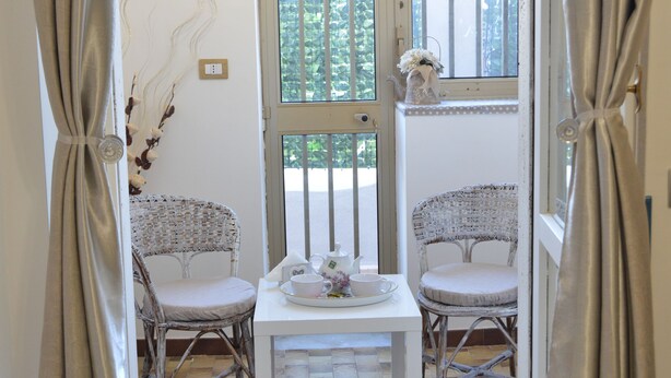 A room with two wicker chairs, a small table with a teapot and cups, and a window with a view of greenery. - Bellatrix (Portici)