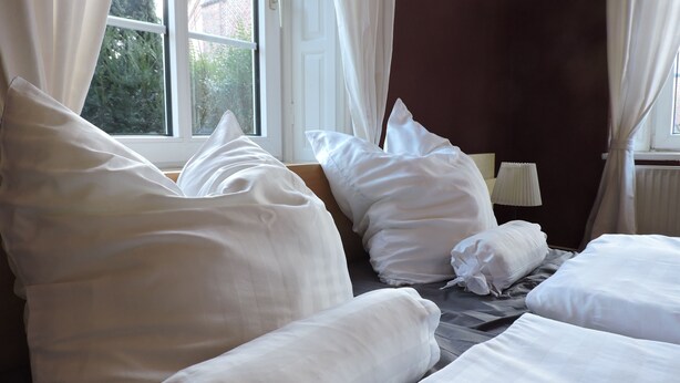 Una habitación de hotel con cama, almohadas, ventana y cortinas.