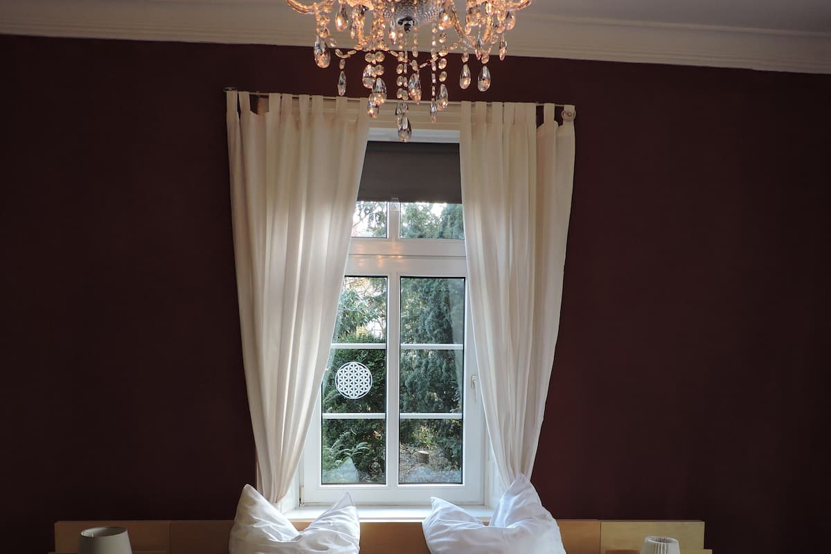 Ein Doppelbett mit weißen Leinen, eine Kristallleuchter und ein Fenster mit Vorhängen.