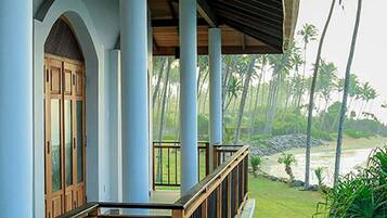 A covered balcony with wooden railings, a pool, and a view of palm trees and a beach.