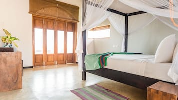 Ein Schlafzimmer mit einem Himmelbett, einem Holzschrank, einem großen Fenster mit Blick und einer gewebten Matte auf dem Boden.