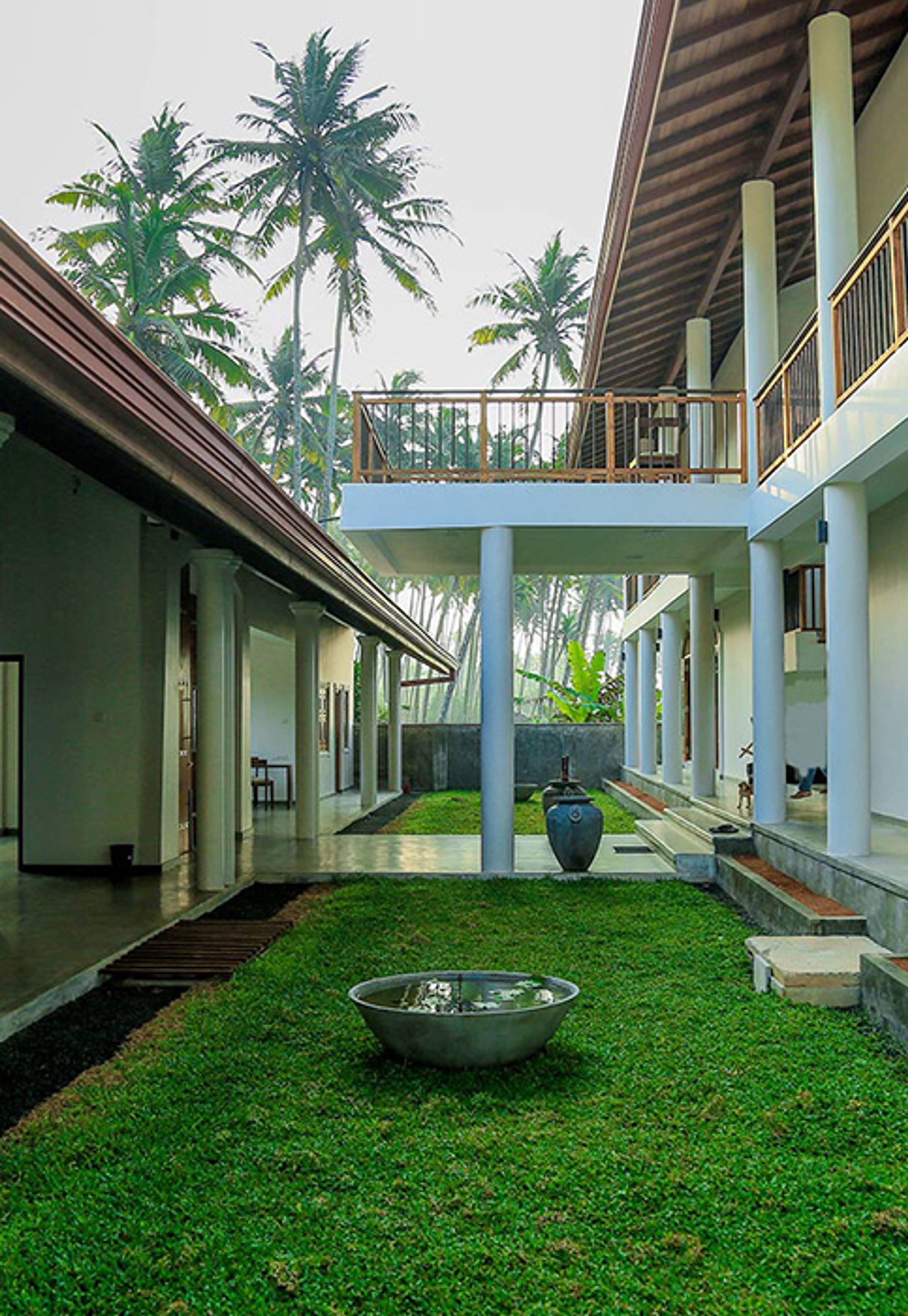 A covered courtyard with a central water feature, palm trees, and a two-story building with a balcony.