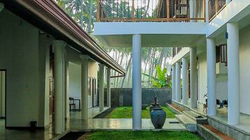 A covered courtyard with a central water feature, palm trees, and a two-story building with a balcony.