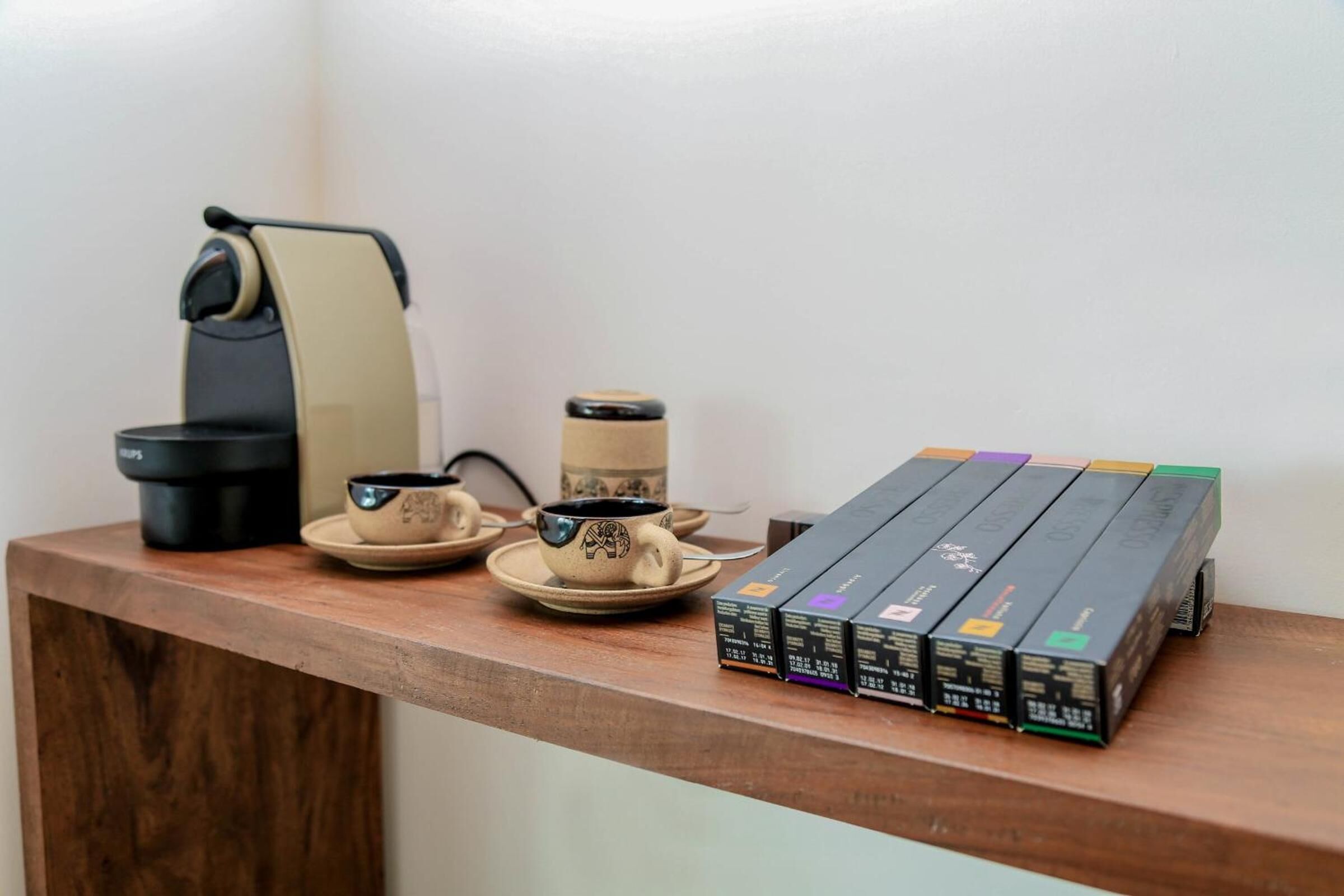 A wooden shelf with a coffee maker, a cup, a saucer, and a box of coffee pods.