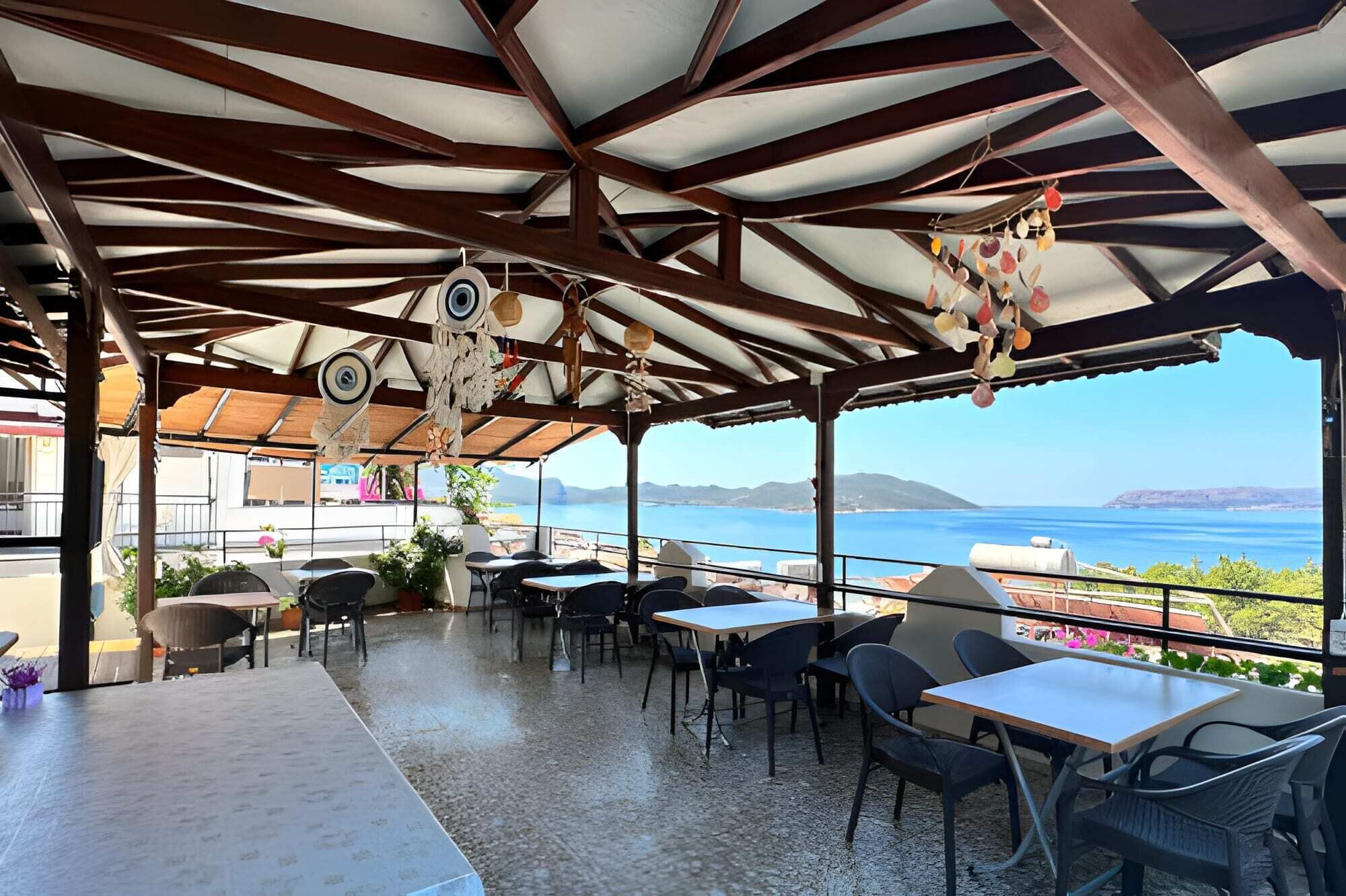 An outdoor seating area with tables and chairs, a view of the sea, and a mountainous landscape in the background.