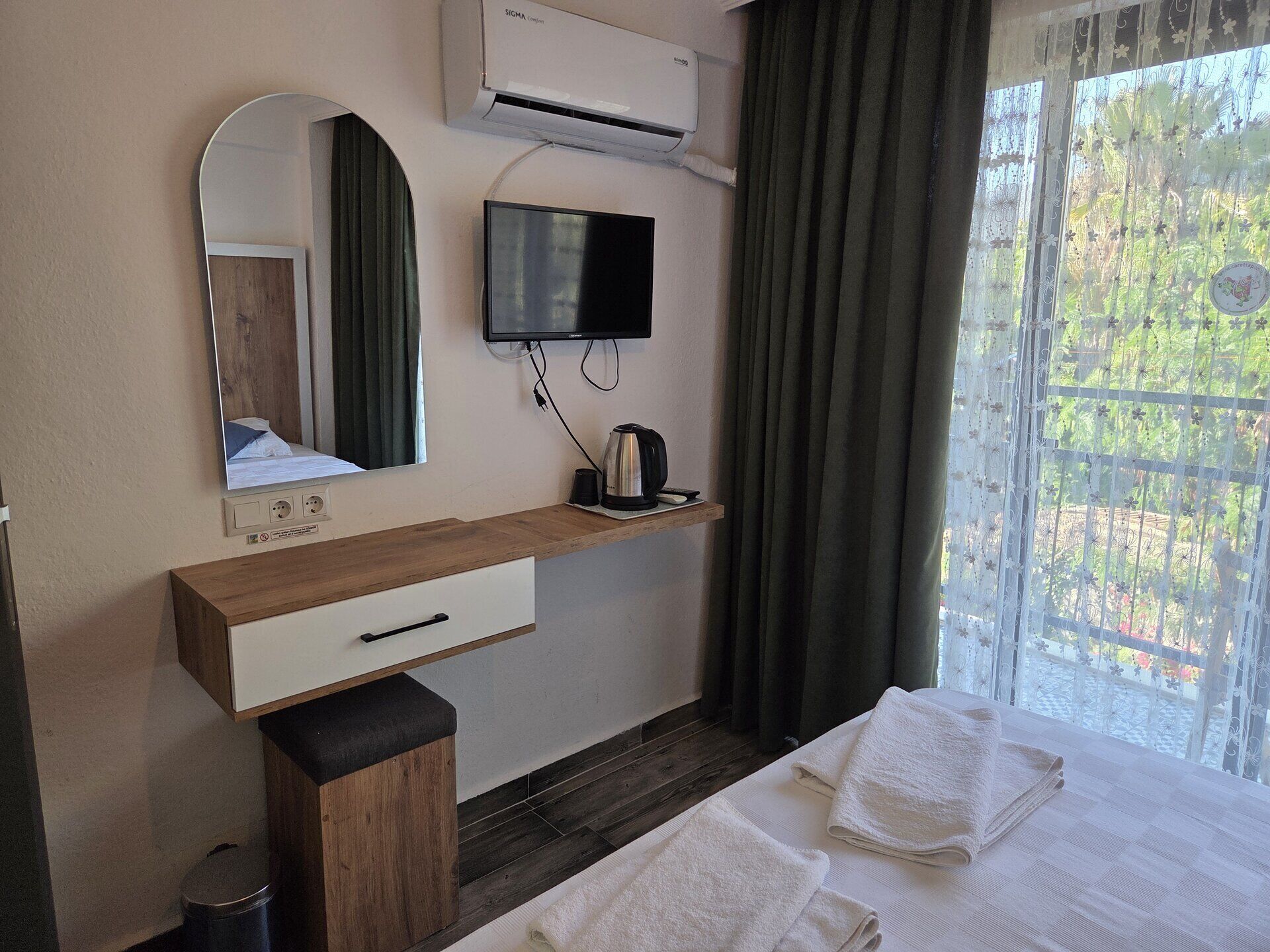 Habitación de hotel con un escritorio de madera, televisión, espejo, ventana con cortinas y cama con toallas.