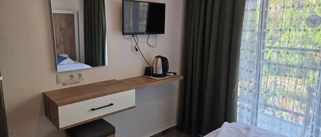 Habitación de hotel con un escritorio de madera, televisión, espejo, ventana con cortinas y cama con toallas.