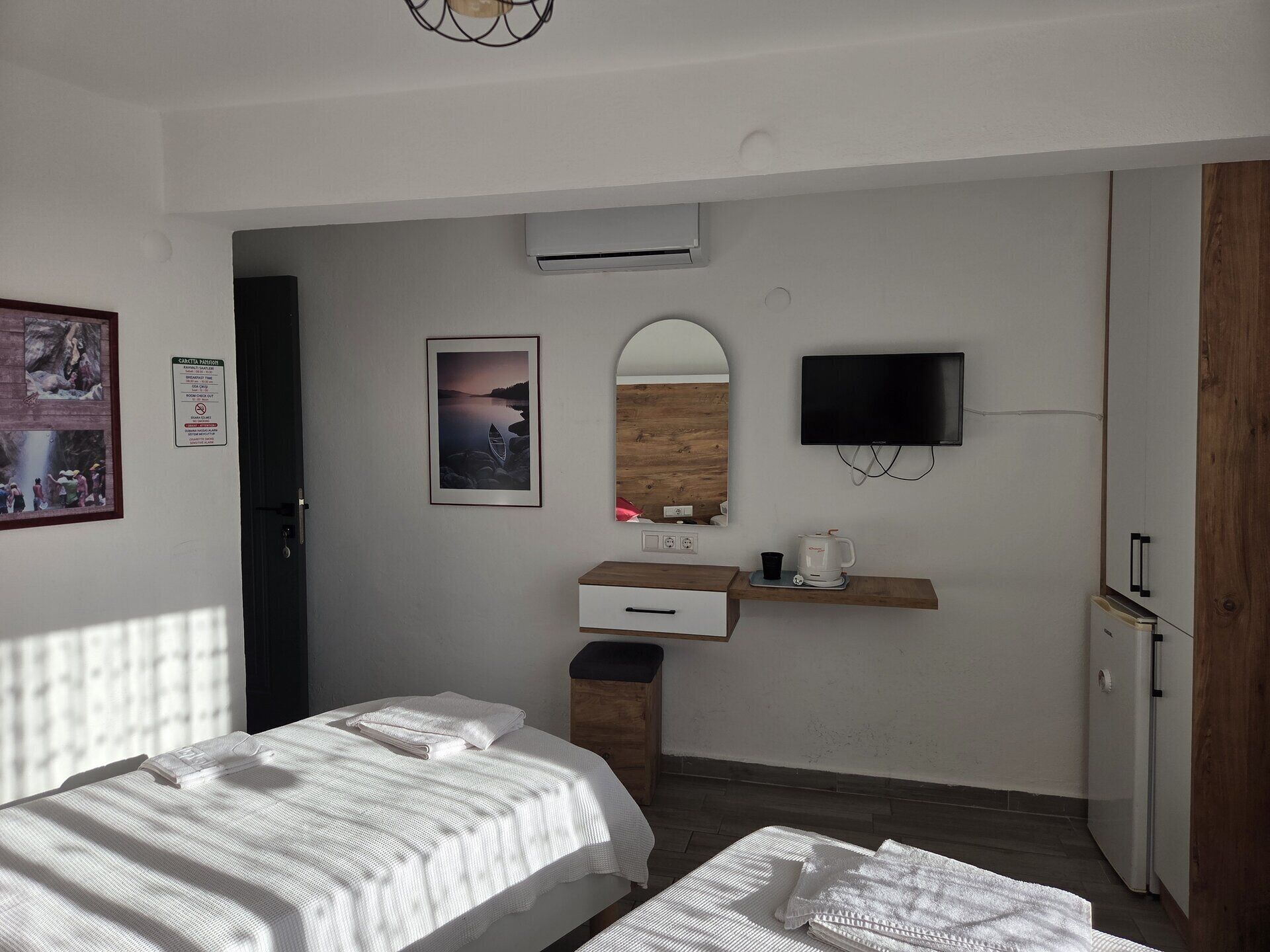 Habitación de hotel con dos camas, televisión, espejo, pequeño escritorio con cafetera y una imagen de una playa.