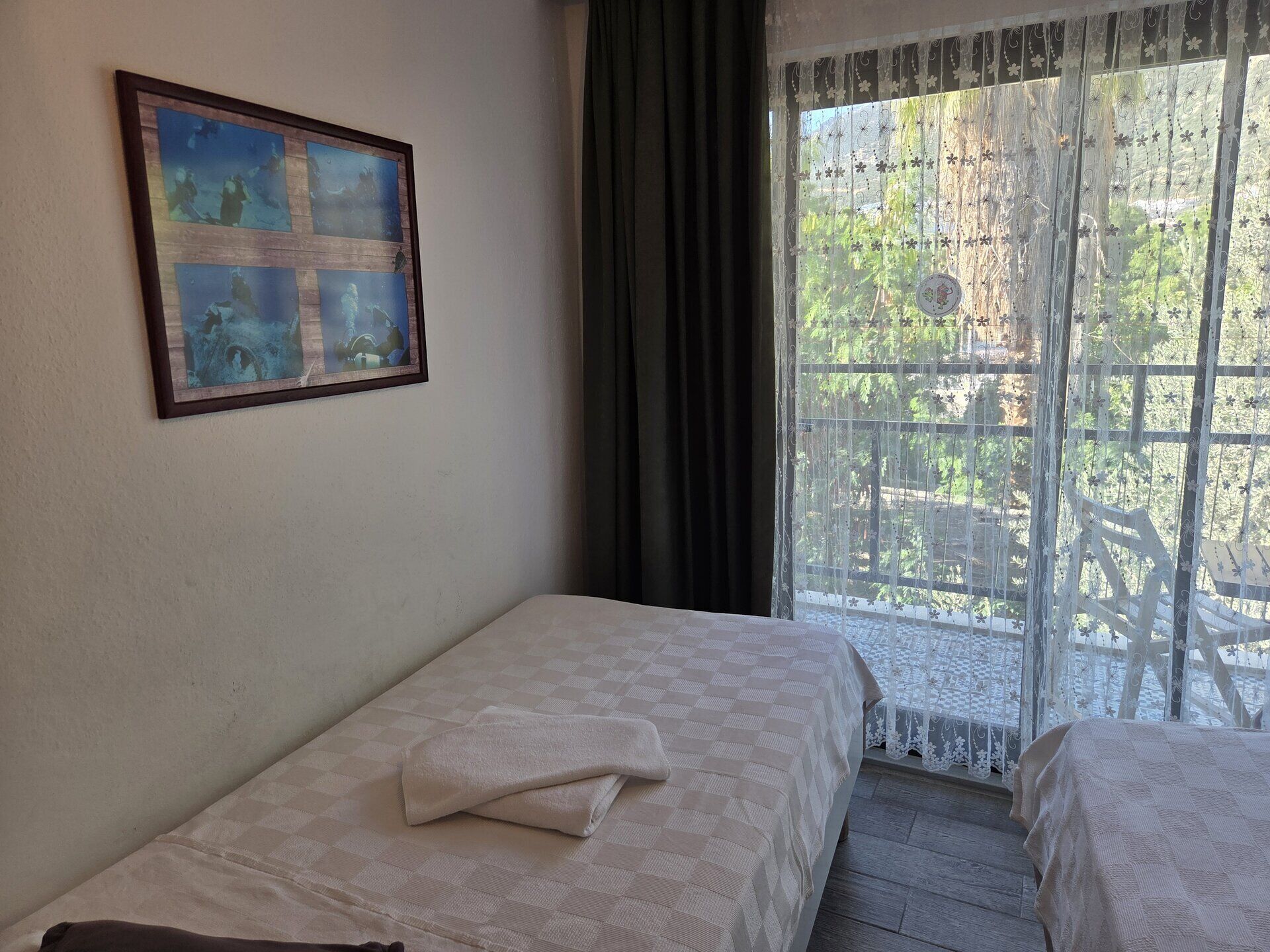 A room with two beds, a framed picture on the wall, and a view through a window with a lace curtain.