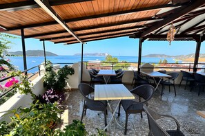 An outdoor seating area with tables and chairs, overlooking a body of water and distant land. - Caretta Pansiyon (Kas)