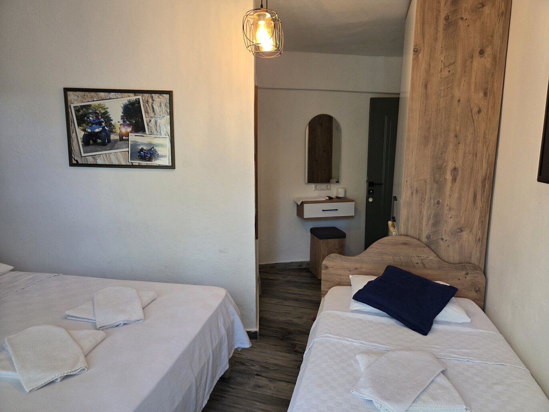 Une chambre avec deux lits, une tête de lit en bois, une petite table de chevet, un miroir et un tableau encadré au mur.
