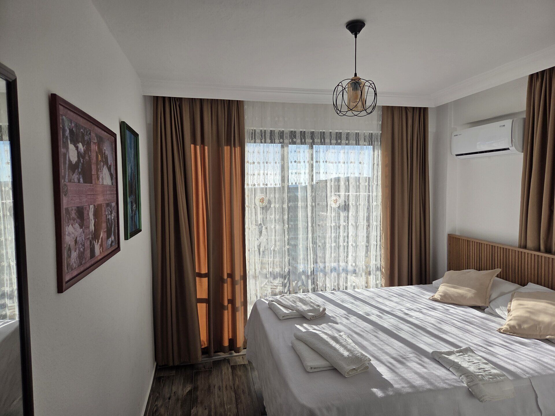 A hotel room with a bed, curtains, a hanging light fixture, and an air conditioning unit.
