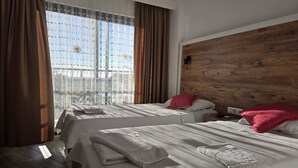 Habitación de hotel con dos camas, cabecera de madera, ventana con cortinas y mesita de noche.