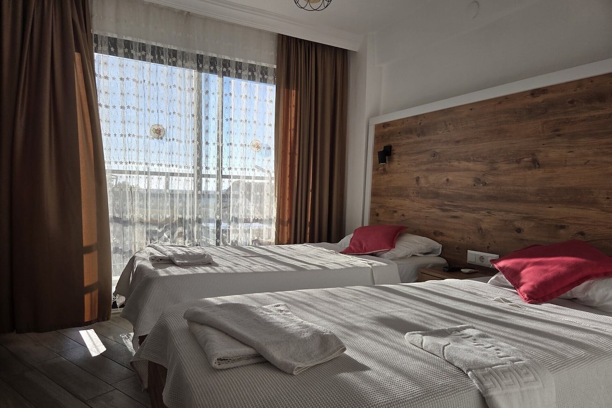 Hotellihuone, jossa on kaksi sänkyä, puinen pääty, ikkuna, jossa on verhot, ja yöpöytä.