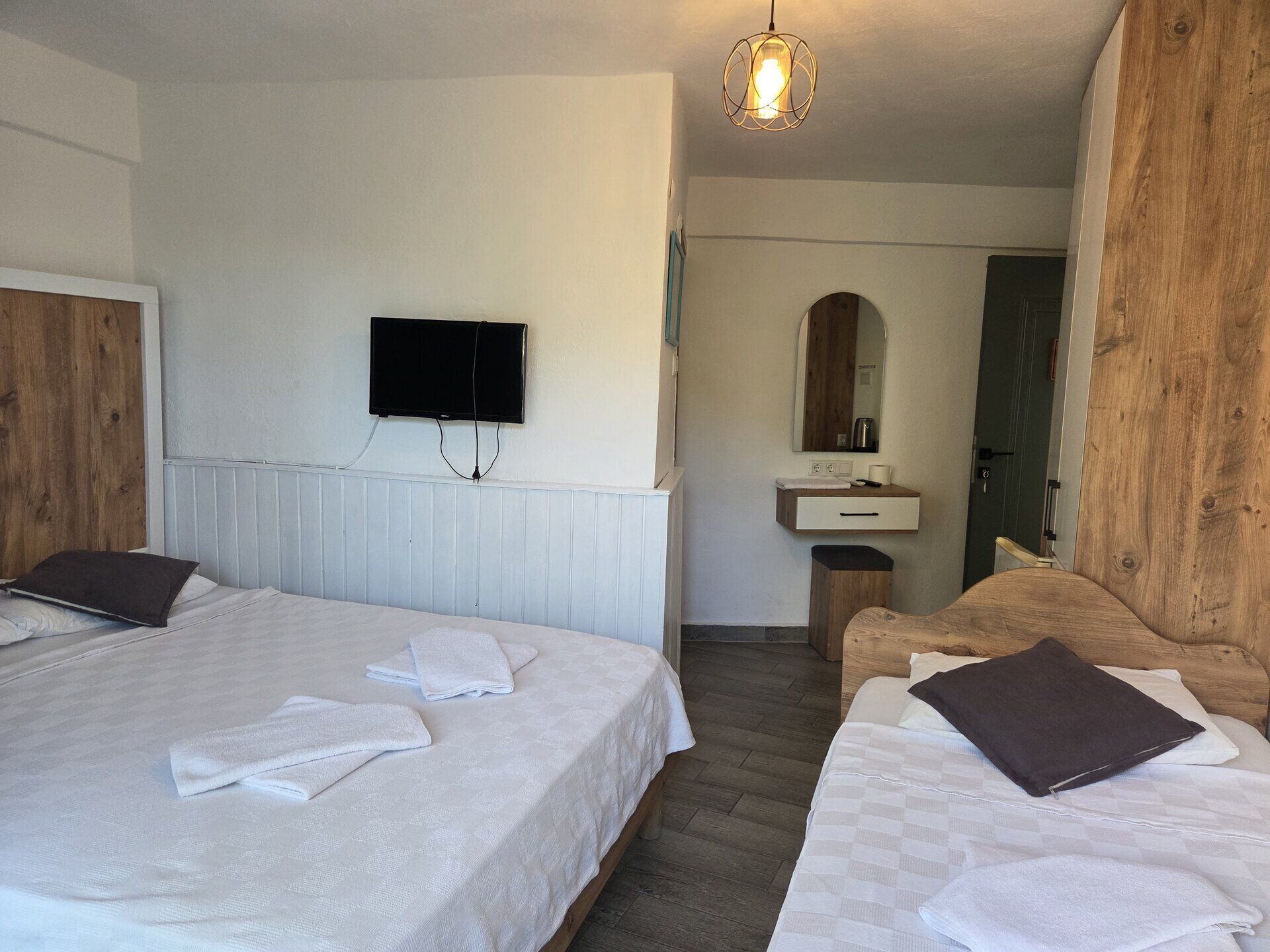 Habitación de hotel con dos camas, televisión, espejo, pared de madera y un baño pequeño.