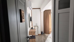 Una habitación de hotel con cama, escritorio de madera, espejo, armario y ventana con cortinas.