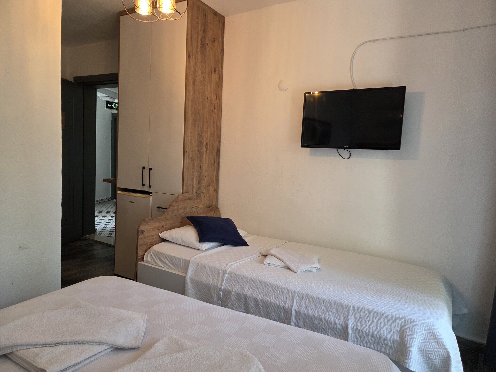 Ein Zimmer mit zwei Betten, einem an der Wand montierten Fernseher und einer Wand mit Holzverkleidung.