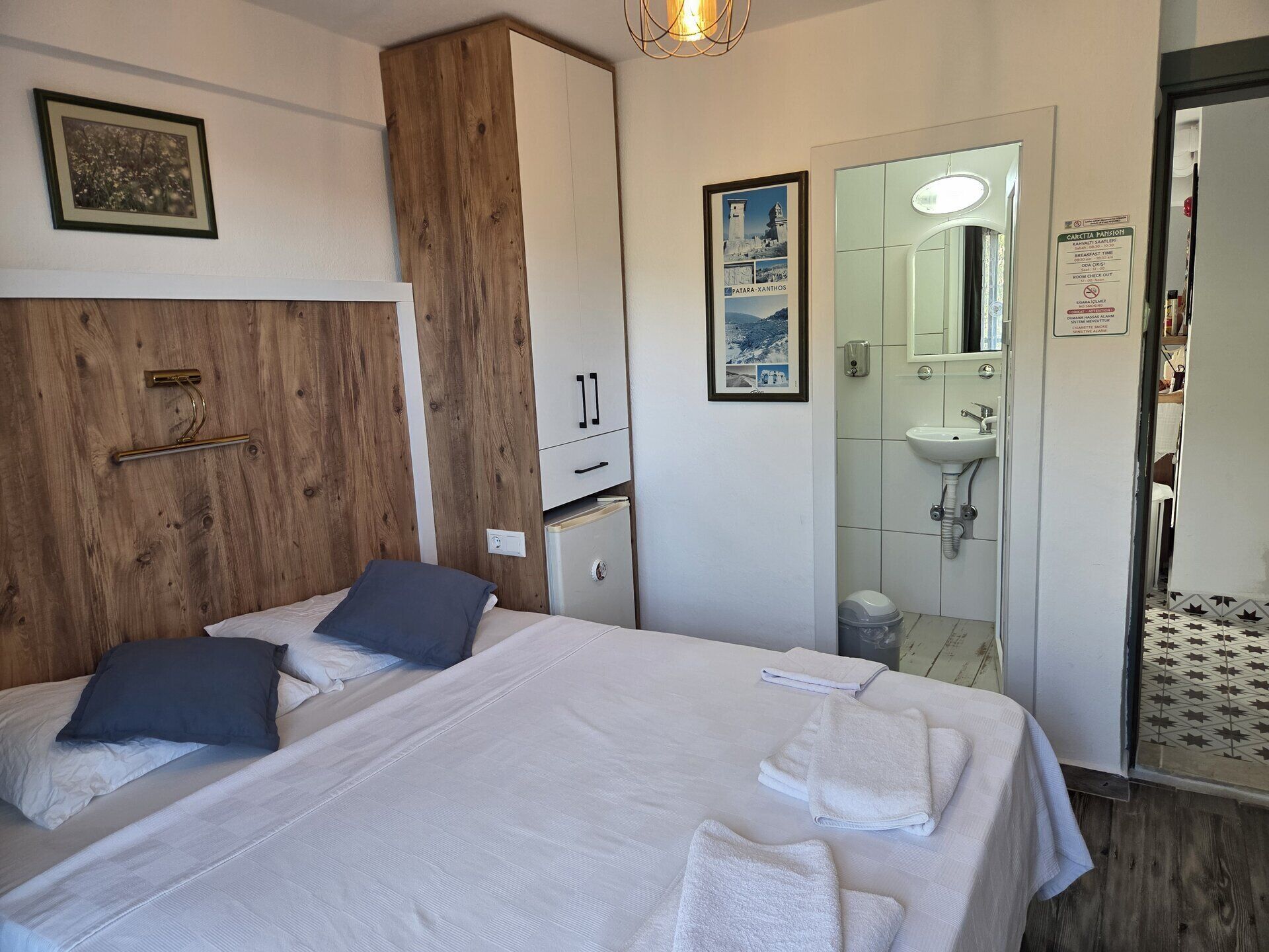 A hotel room with two beds, a wooden headboard, a framed picture, a mirror, a sink, and a poster on the wall.