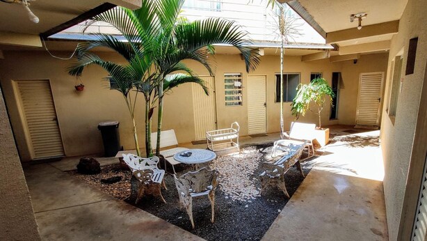 Un patio techado al aire libre con una mesa y sillas, rodeado de palmeras y un suelo de hormigón.