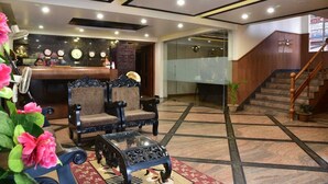 A lobby with a reception desk, two armchairs, a coffee table, and a staircase. - Hotel Venkatesh Regency (Siliguri)