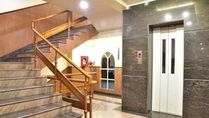 A staircase with wooden handrails leading to an elevator. - Hotel Venkatesh Regency (Siliguri)