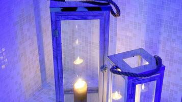 Due lanterne di vetro con candele all'interno, posizionate su un pavimento piastrellato davanti a un muro rivestito in piastrelle.