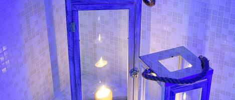 Two glass lanterns with candles inside, placed on a tiled floor against a tiled wall.