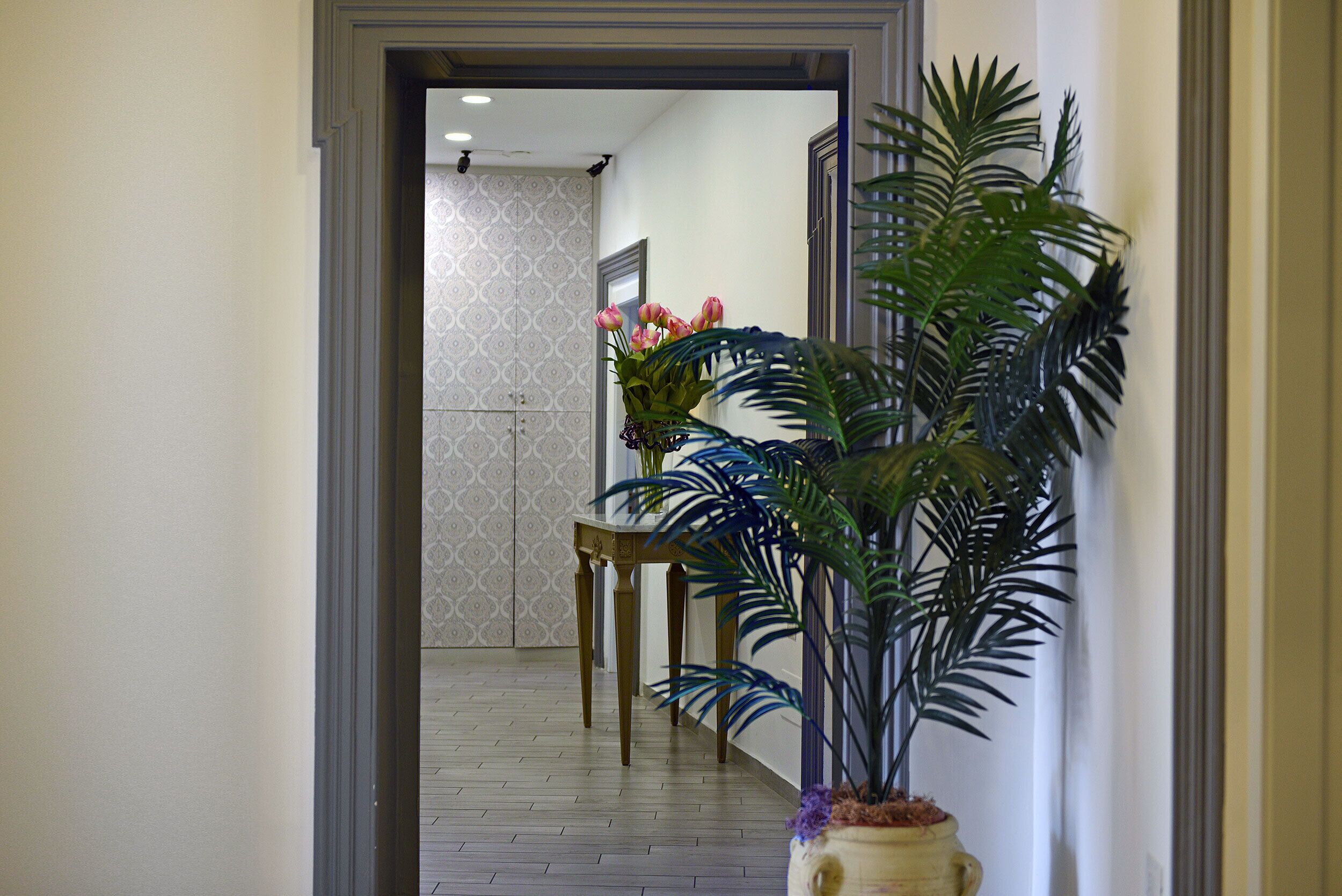 A hallway with a wooden floor, a potted plant with green foliage, and a table with a vase of flowers.
