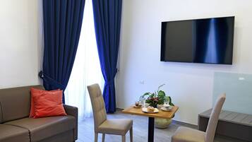 Un soggiorno moderno con divano, due poltrone, un tavolo da pranzo con una pianta e una televisione a schermo piatto montata a parete.