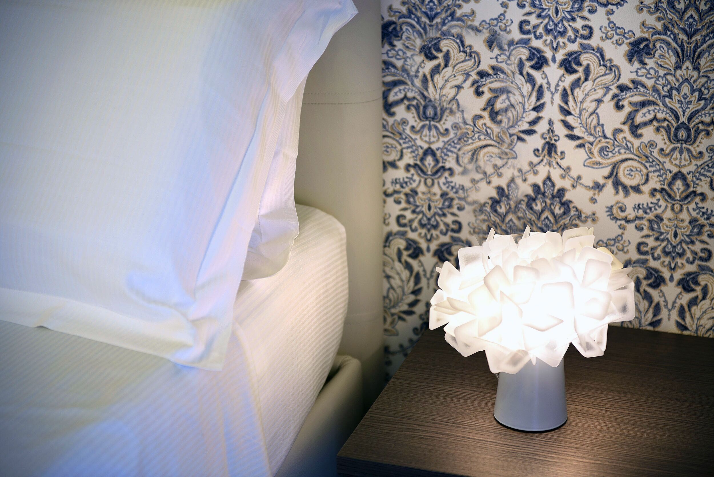 Un comodino con un vaso bianco e una lampada decorativa accesa.
