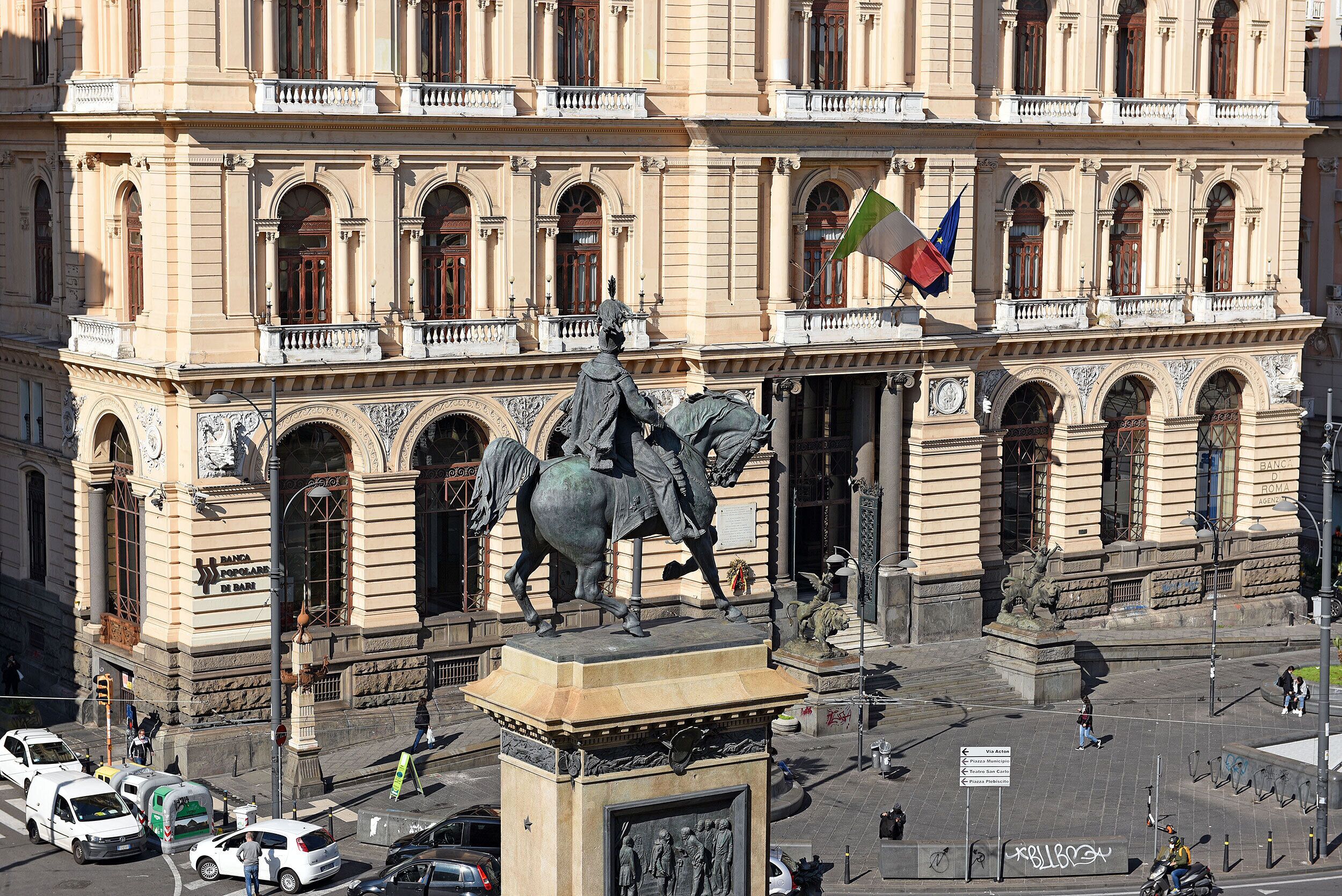 A statue of a man on horseback in front of a large building with multiple arches and columns.