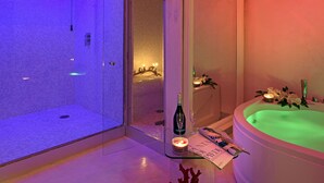 Un baño moderno con ducha envuelta en vidrio, una bañera independiente y una mesa de vidrio con una vela y una botella.
