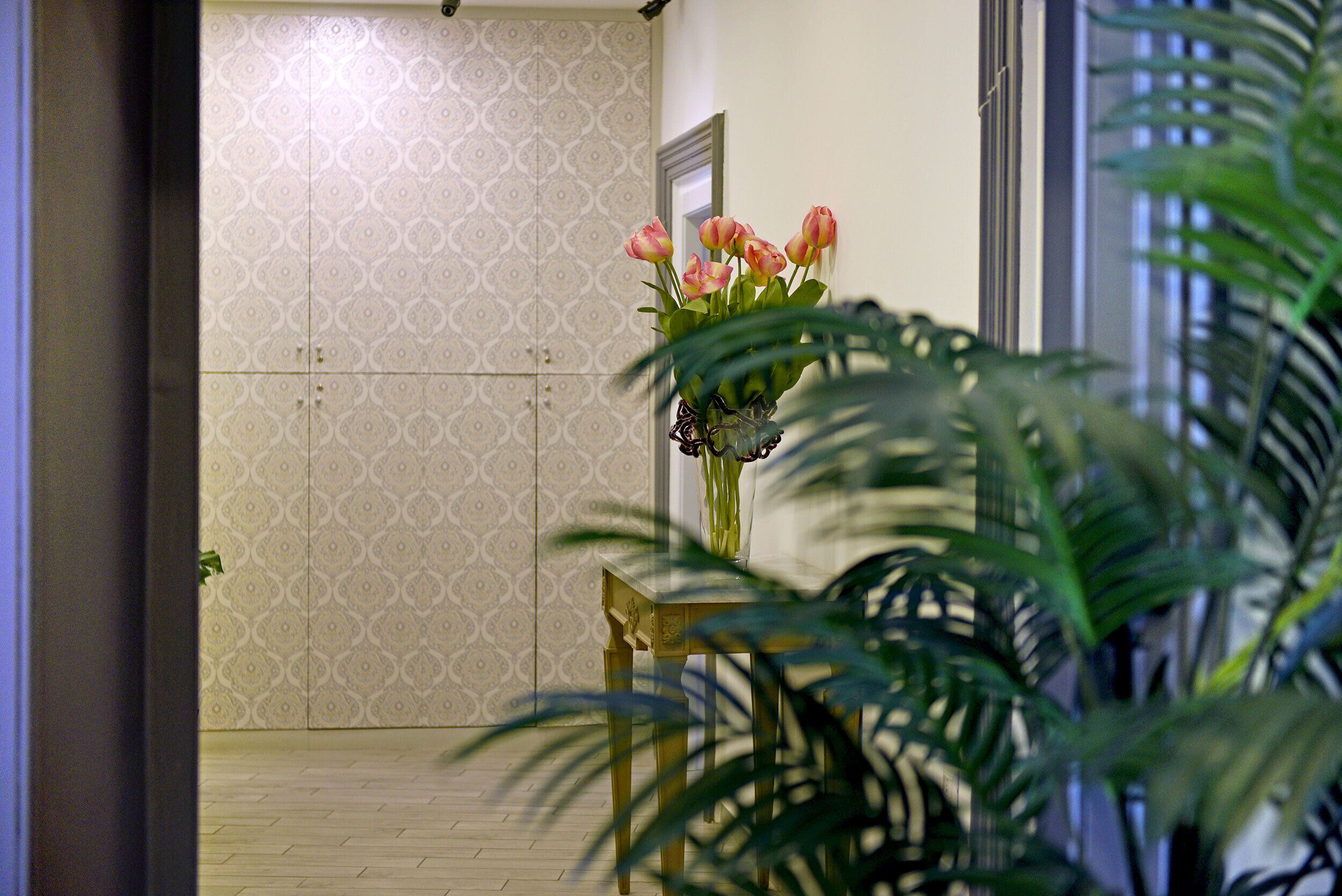 A room with patterned wallpaper, a wooden table, and a vase with flowers.