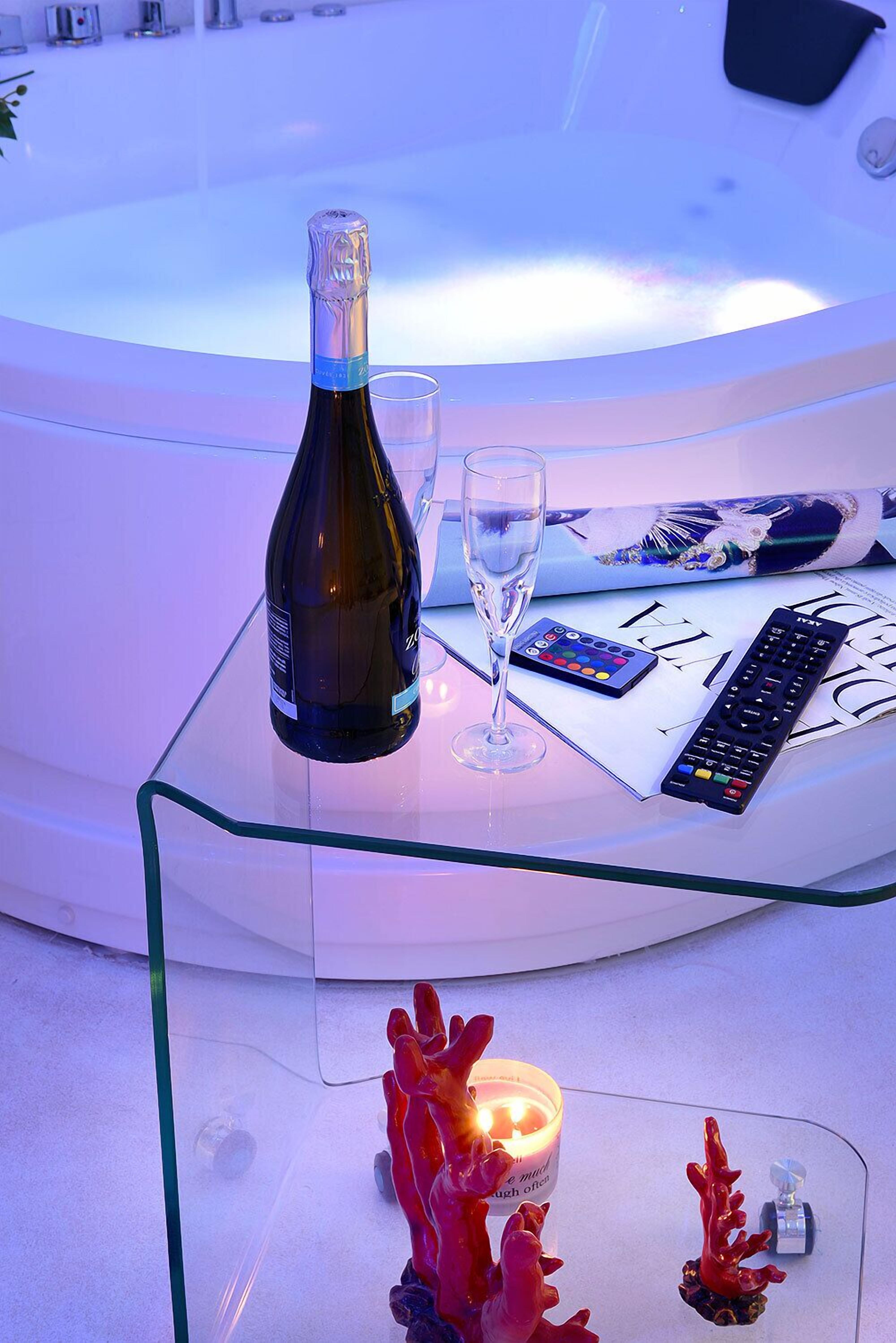 A glass table with a bottle of champagne, a glass, a remote control, and a magazine.