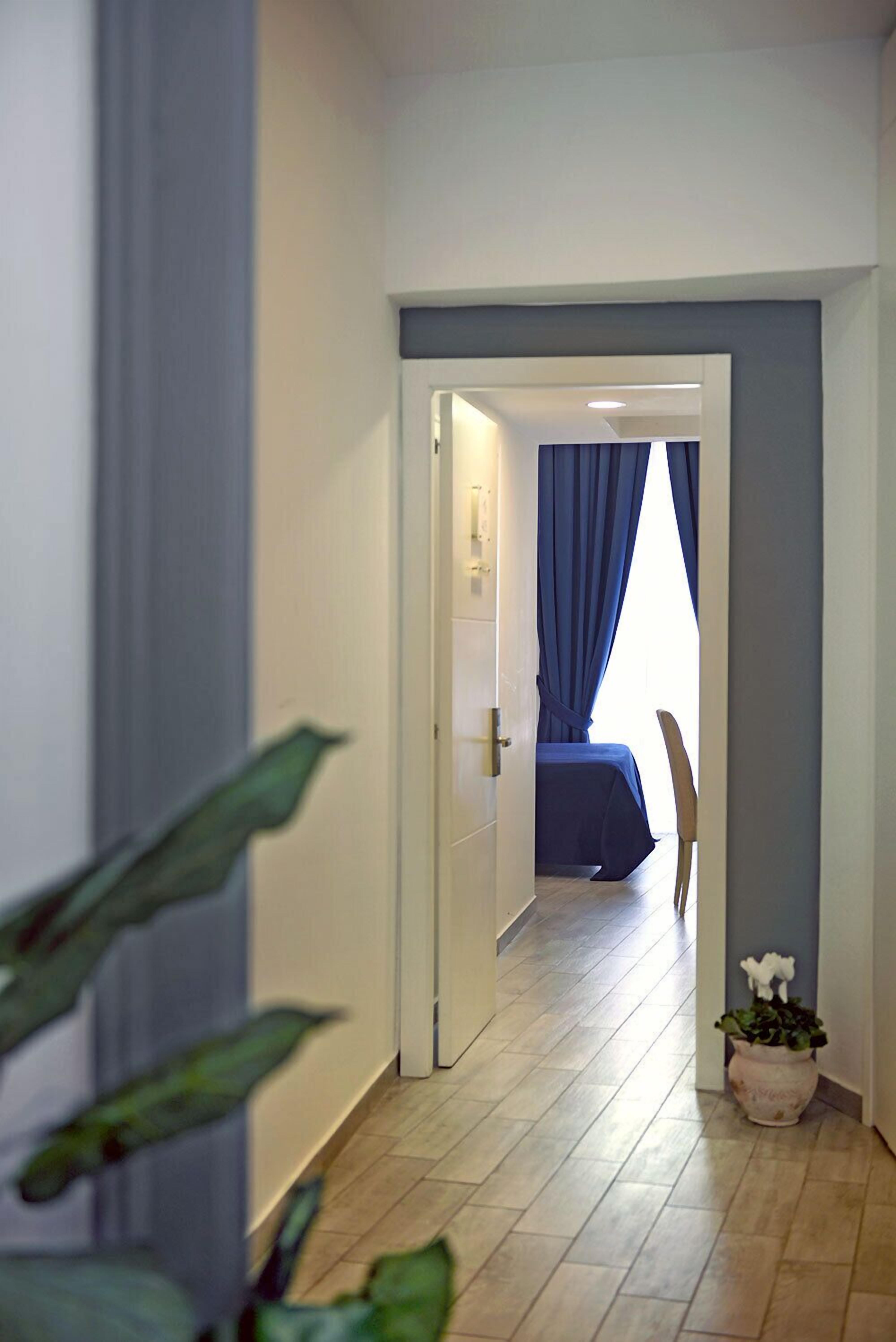 Un pasillo que conduce a un dormitorio con una cama, una planta en maceta y una puerta con cortina.