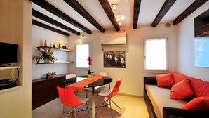 Un espacio de estar moderno con comedor, sofá con cojines rojos y televisor a la izquierda.