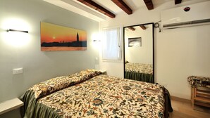 Un dormitorio con cama, mesita de noche, espejo y un cuadro de un atardecer.